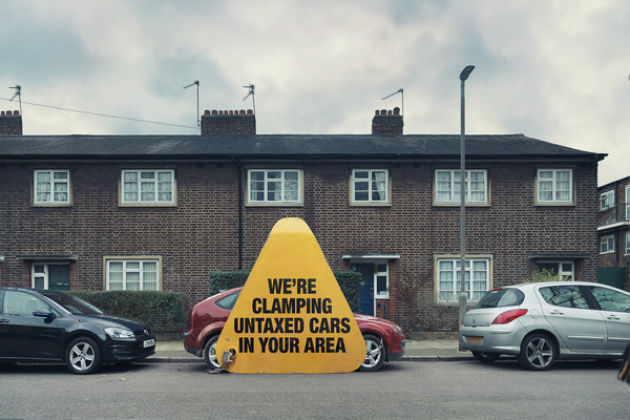 A large yellow triangle in front of a car informing residents that clamping is occurring within this area.