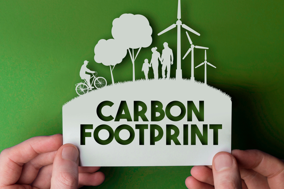 White sign with with two trees, a bike, a family, and three wind turbines with a saying below: 'carbon footprint', all in the green background.
