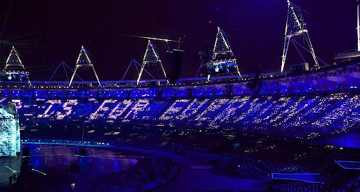 A busy stadium at night with the words "This is for everyone" illuminated by the crowd.