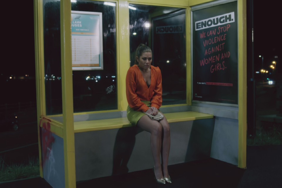 A woman sitting on her own at a dark bus stop.