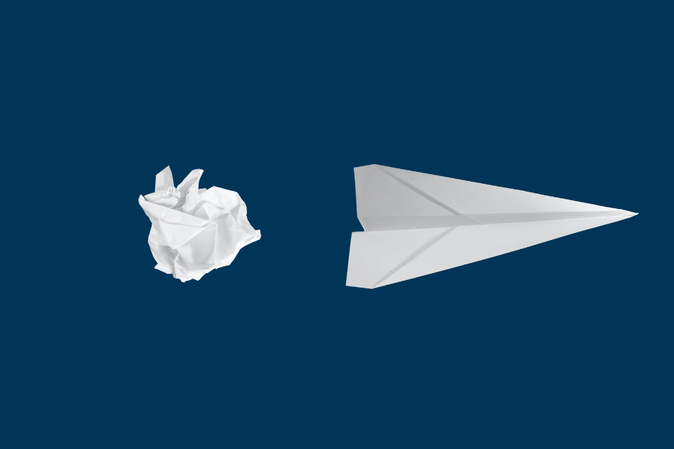 white scrunched up paper ball and folded paper aeroplane on a blue background