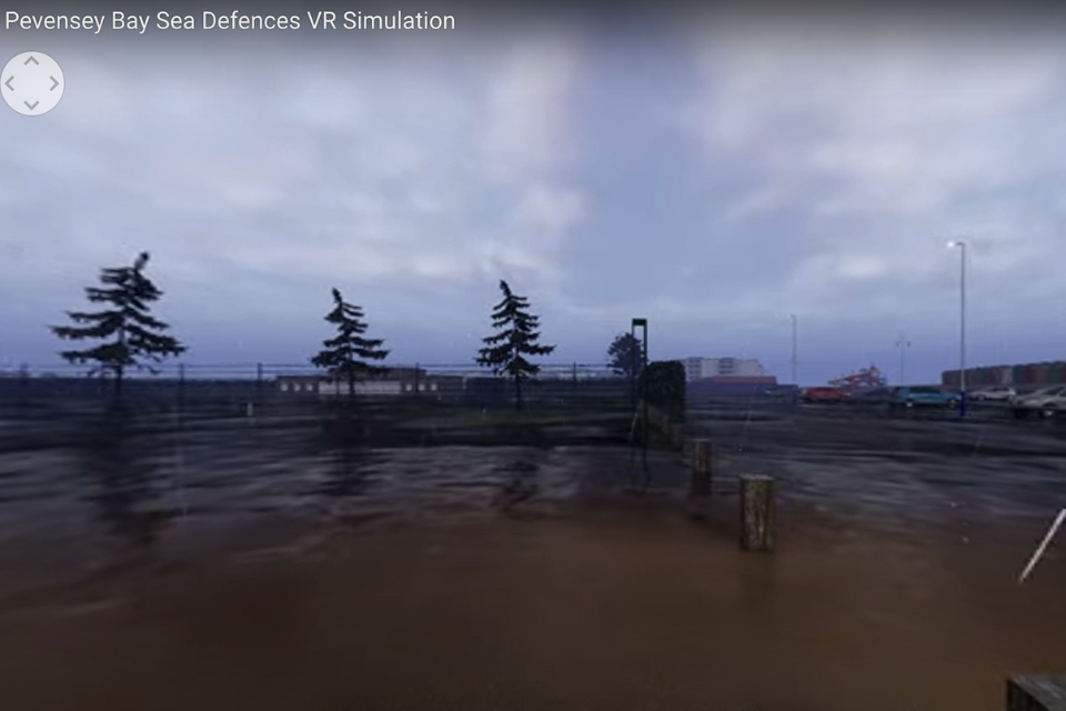 A still of a virtual reality simulation set by the English coastline, showing the sea level rising and the land being covered by water. There are two buildings in the distance underwater.