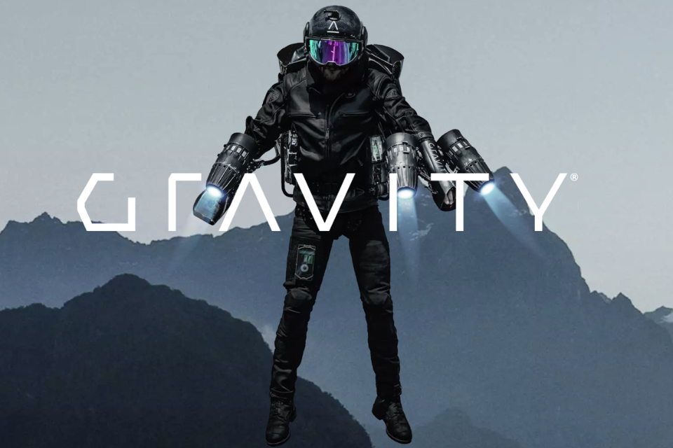 A person suspended in the air in front of mountains, wearing a helmet, eye shield and black clothing, and powered by engines on each arm. Text across the image reads, ‘ Gravity'.